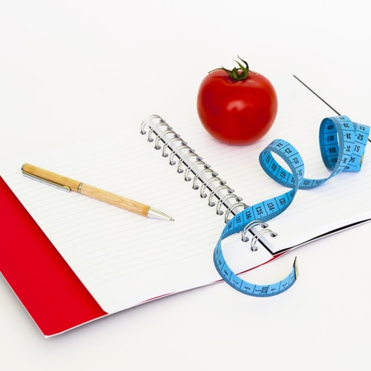 a notebook with a tomato and measuring tape designed to track food intake for an inflammation diet.
