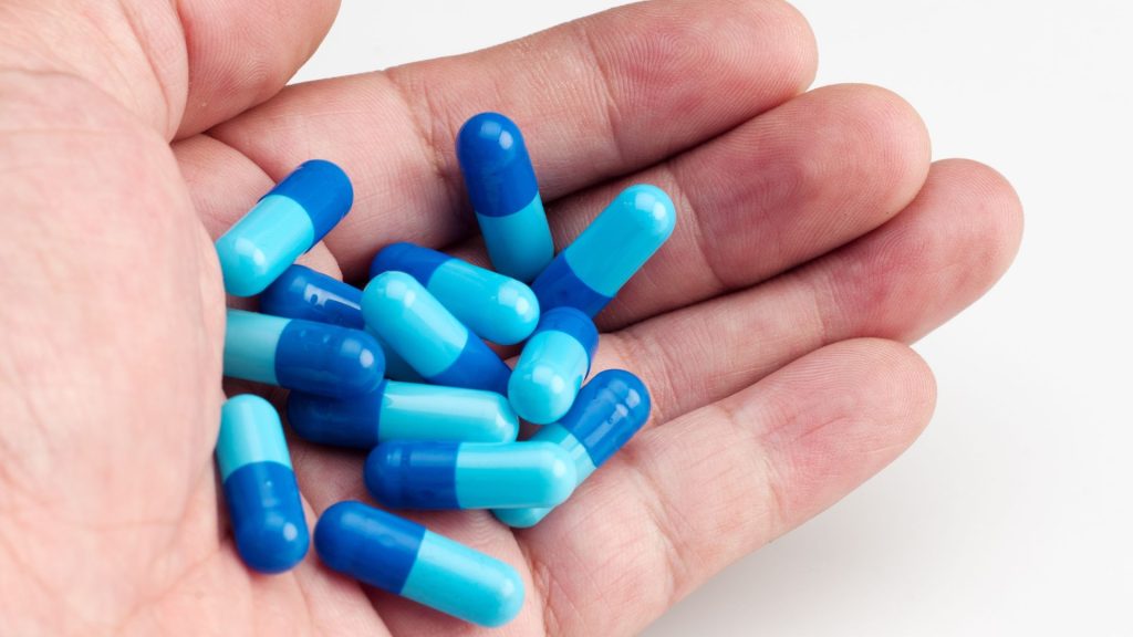 a person's hand holding a bunch of blue pills emitting a faint hs odor.