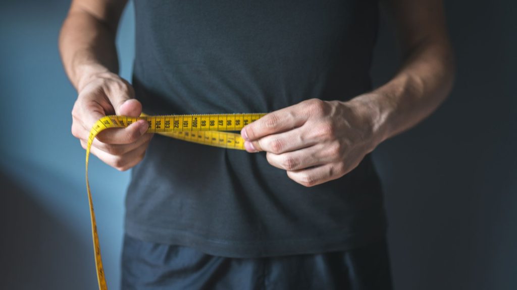 a man engaged in healthy living is measuring his waist with a measuring tape.