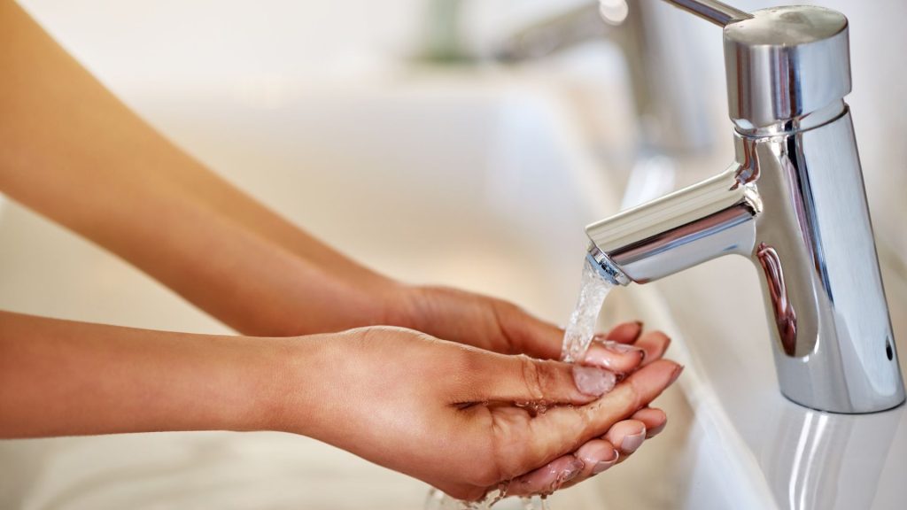 a person practicing healthy living by washing their hands under a running water faucet.