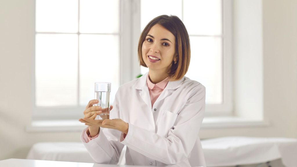 a woman in a lab coat promoting the importance of healthy lifestyle habits while holding a glass of water.