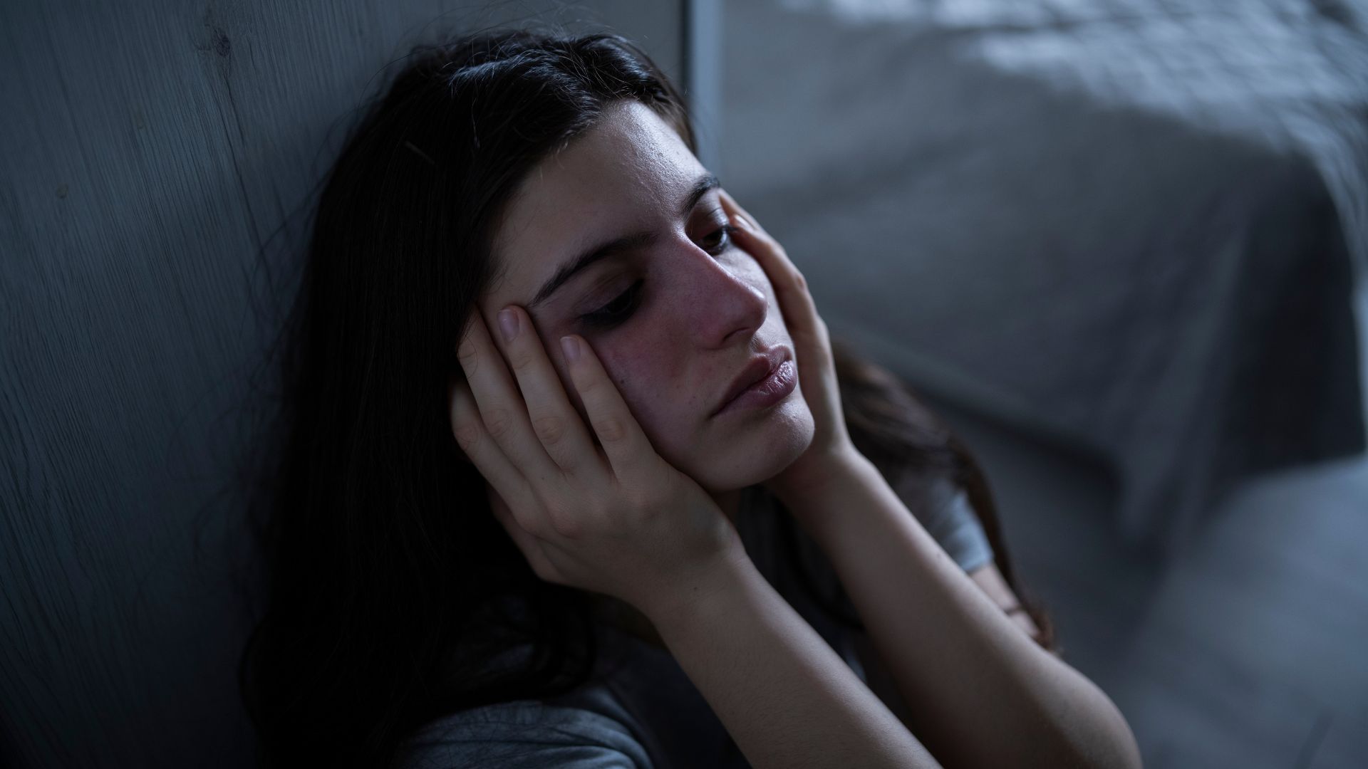 A woman with her hands on her face in a dark room, struggling to understand misconceptions about Hidradenitis Suppurativa