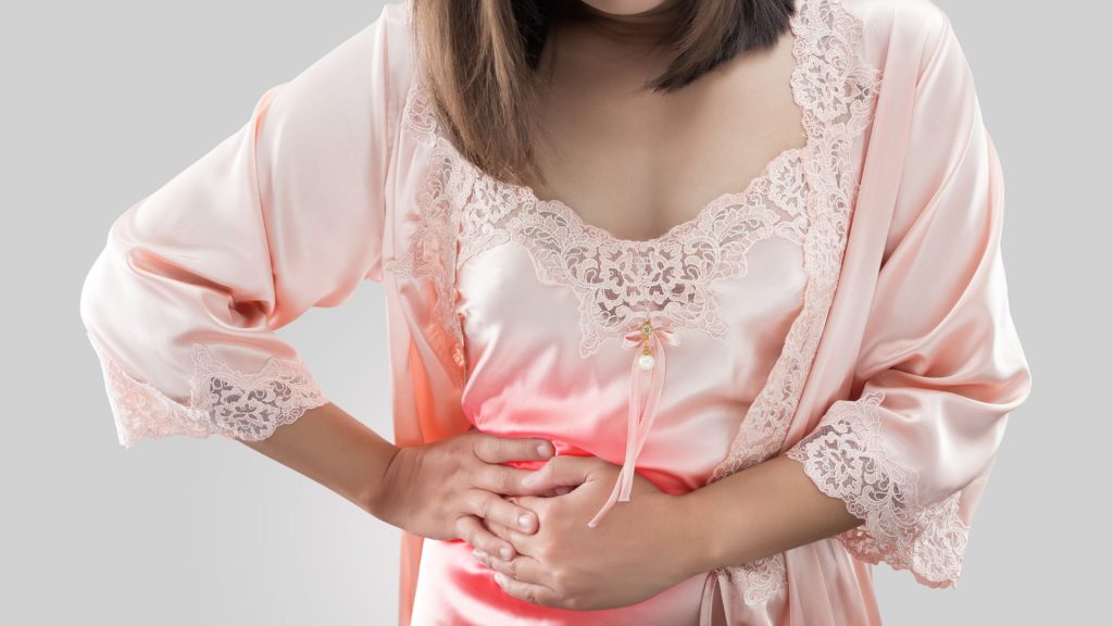 a woman in a pink nightgown experiencing discomfort in her stomach, possibly indicating a potential risk of hidradenitis suppurativa.