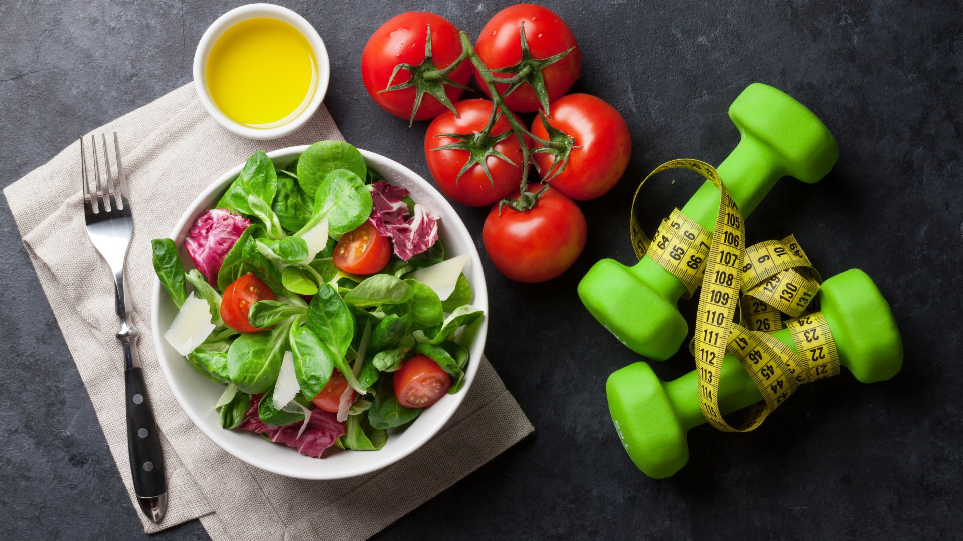 A healthy bowl of salad packed with nutritious tomatoes, accompanied by a pair of dumbbells for a balanced health nutrition and fitness routine.