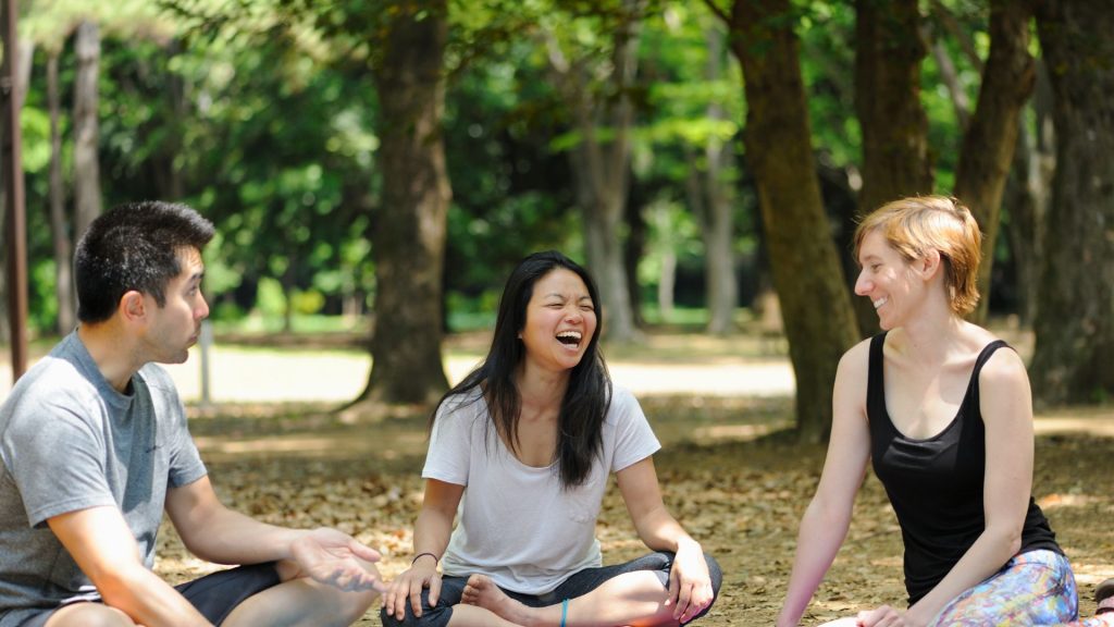 a group of people laughing in a park, showcasing the positive impact laughter has on psychological health.