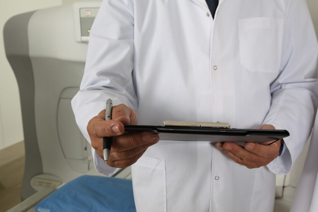 a person in a white coat holding a clipboard and pen conducts research on hidradenitis suppurativa autoimmune condition.