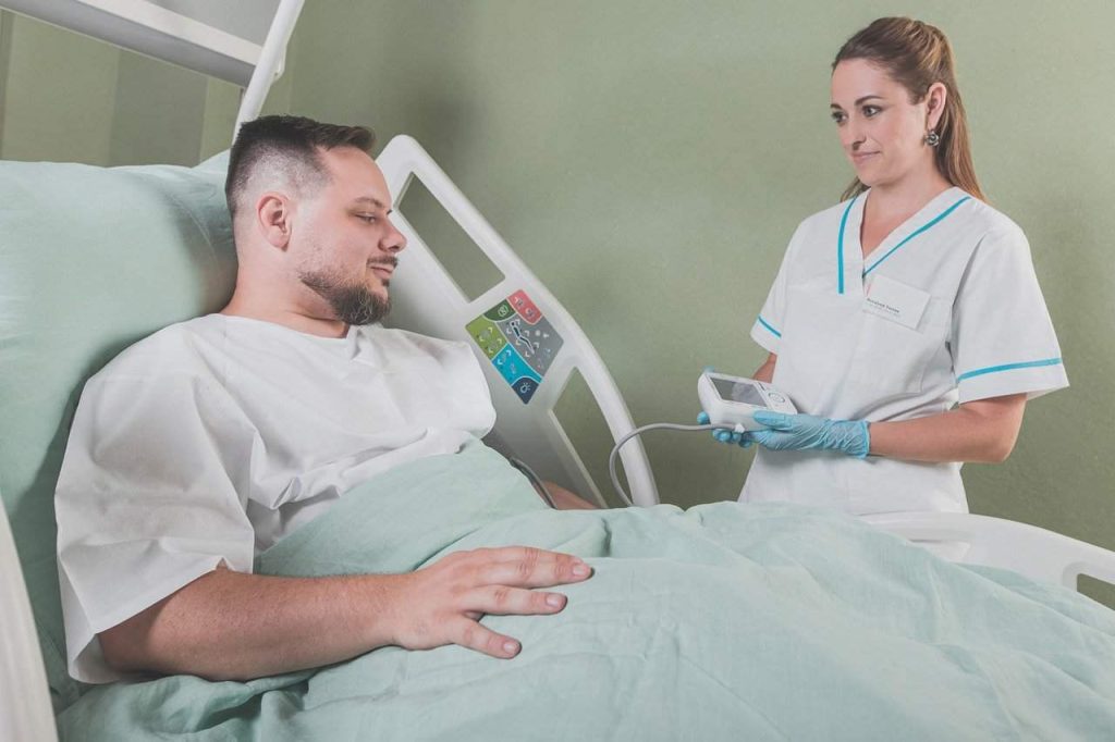 a nurse in a white uniform checks the vitals of a male patient living with hidradenitis suppurativa, lying in a hospital bed, using a medical device.