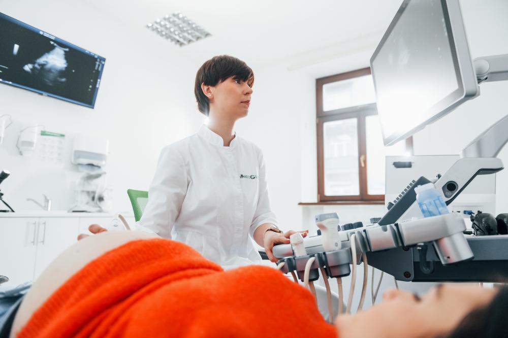 a medical professional is performing an ultrasound examination on a patient lying down, using a monitor and specialized equipment in a white clinical room, while discussing the potential benefits of laser therapy for hs.