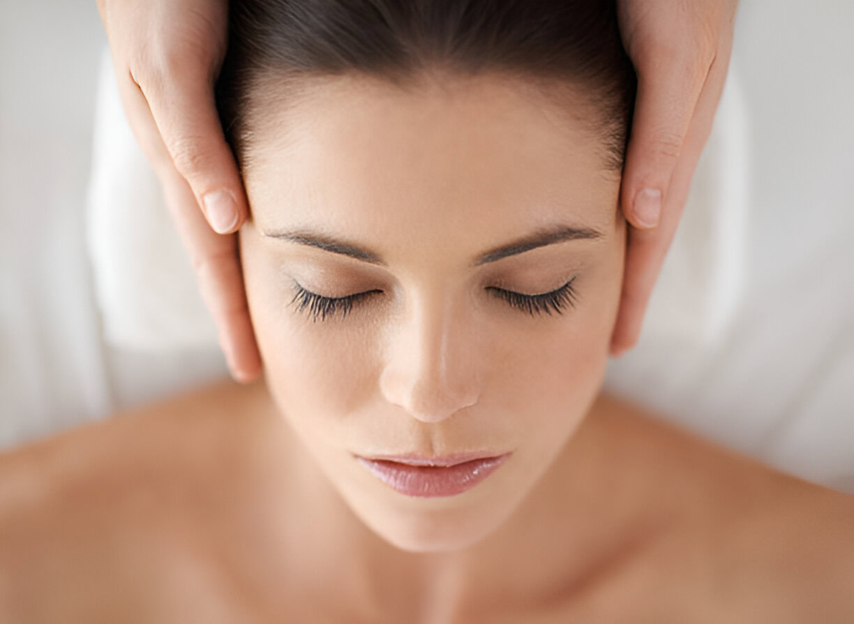 A person with closed eyes receiving a head massage, with hands on both sides of the head, lying down in a relaxed position.